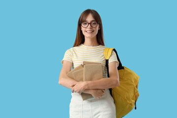 Fototapeta premium Happy female student with books and backpack on blue background