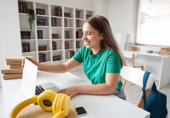 Happy female student with books, headphones and laptop studying at library