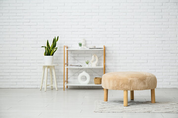 Pouf, shelving unit and houseplant near white brick wall in room