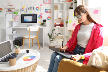 Female graphic designer working with tablet in armchair at office