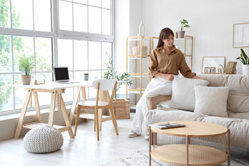 Pretty young woman putting pillow on sofa