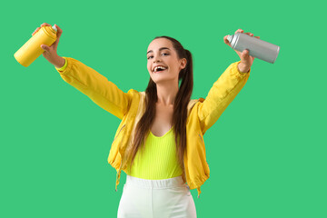 Young woman with spray paint cans on green background