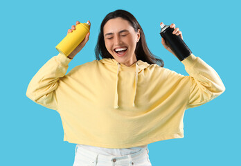 Happy young woman with spray paint cans on blue background