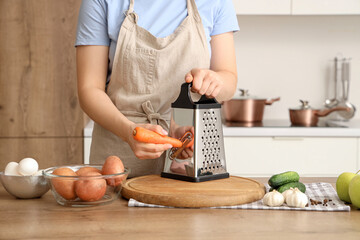 Woman grating carrot at table in kitchen, closeup