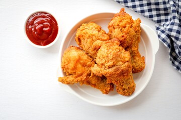 Fried chicken on a white plate with tomato sauce on white background, top view food table
