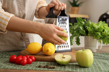 Woman grating apple at table in kitchen, closeup