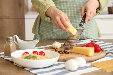 Woman grating cheese onto board at table in kitchen, closeup