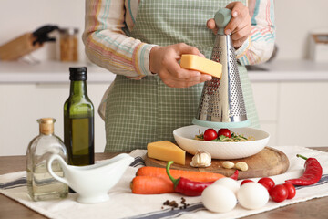Woman grating cheese onto pasta at table in kitchen, closeup