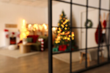 Blurred view of festive living room with green sofa, glowing lights and Christmas tree, view through partition