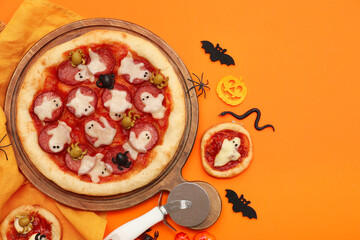 Composition with tasty pizzas, cutter and decorations for Halloween on orange background