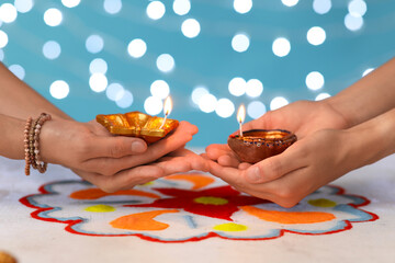 Female hands with diya lamps for Diwali and colorful powder on white table against blue blurred background