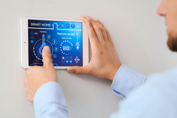 Young man using smart home control panel on light wall in room, closeup