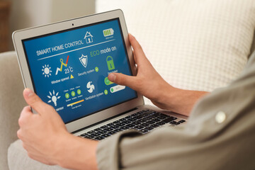 Young man using laptop with smart home application in room, closeup