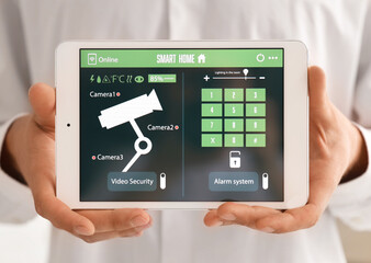 Young man with smart home security system control panel in kitchen, closeup
