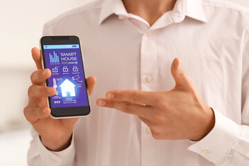 Young man and mobile phone with smart home application in kitchen, closeup