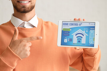 Young man pointing at smart home control panel in room, closeup