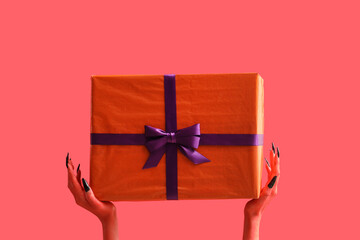 Devil hands with gift box on red background. Halloween celebration