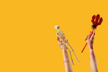 Zombie hands with skeleton and devil trident on yellow background. Halloween celebration