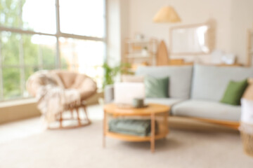Blurred view of light living room with grey sofa and laptop on coffee table