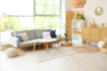 Blurred view of modern living room with grey sofa and coffee table near window