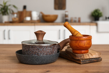 Cooking pot, frying pan, mortar and pestle on wooden counter in kitchen