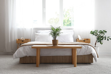 Interior of light bedroom with cozy bed and houseplants near window