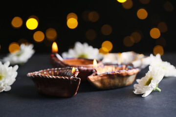 Diya lamps with flowers against blurred lights on black background. Divaly celebration