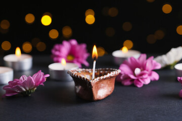 Diya lamp with flowers and candles against blurred lights on black background. Divaly celebration