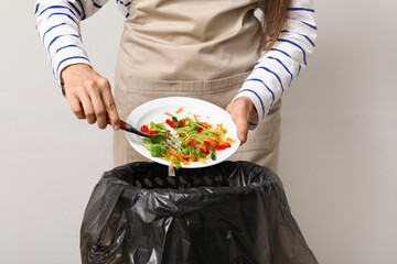 Young woman throwing organic food into trash bin on grey background, closeup. Waste recycling...