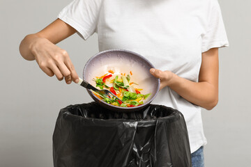 Young woman throwing organic food into trash bin on light background, closeup. Waste recycling...