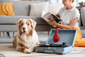 Cute Australian Shepherd dog with record player and owner reading magazine at home