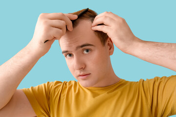 Young redhead man with hair loss problem combing on blue background, closeup