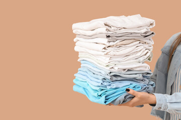 Young woman with stack of clothes on beige background, closeup