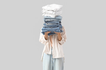 Naklejka premium Young woman with stack of clothes on light background