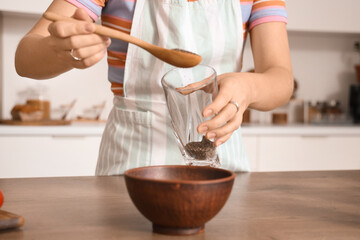 Young woman pouring chia seeds into glass in kitchen, closeup