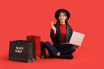 Young woman with laptop and credit card shopping on red background. Black Friday Sale