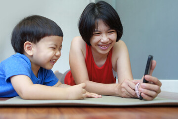 Asian Mother and little child boy lying on yoga mat and looking at a smartphone. Indoor leisure activity. Family bonding and technology concept