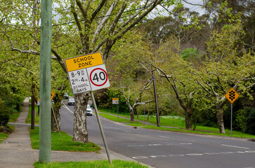 A school zone sign on a tree-lined street beside a road in Melbourne, Australia, indicates a speed...