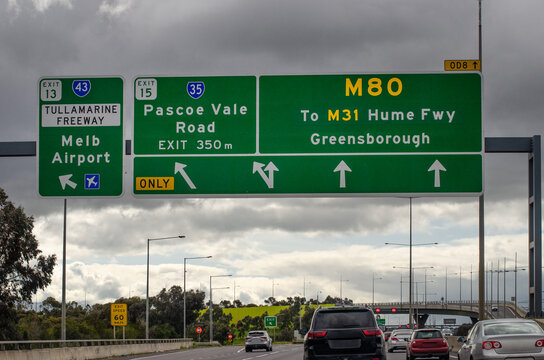 A road sign over a busy Australian freeway indicating the upcoming exit 35 on the M80 highway provides directions to Hume Freeway, Greensborough, and Melbourne Airport.