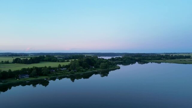 drone footage showing evening view of lake with green fields, windbreaks and blue sky in  Denmark