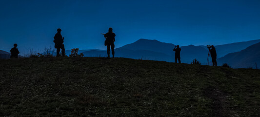 At night, on the top of a hill, there is an area where several people with silhouettes holding weapons and standing guard look into the camera