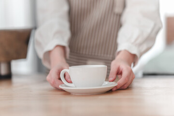 A hands-on approach as a barista presents a white coffee cup on a saucer against a warm, inviting background.