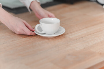 A person is placing a white coffee cup on a wooden table, emphasizing a cozy and inviting coffee moment.