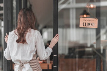 A woman stands outside a closed café, facing the door with a "CLOSED" sign visible, suggesting the establishment is no longer open for business. © phaitoon