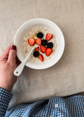 A woman's hand holds a plate of oatmeal porridge with fresh strawberries, blackberries and honey. Delicious healthy breakfast