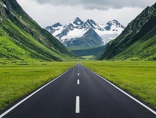 Fototapeta premium Long road leading to snow-capped mountains through lush green valleys.