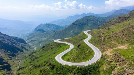 Scenic winding mountain road through lush green hills under a blue sky.