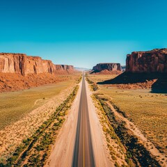 Naklejka premium Straight road cutting through desert landscape with rock formations and blue sky.