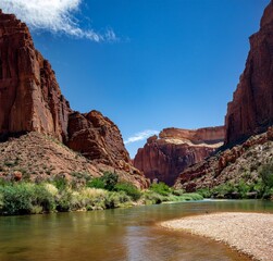 Towering reddish-brown cliffs and a clear river create a stunning canyon landscape. Enjoy lush greenery, palm trees, and the tranquil beauty of this natural oasis