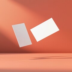 Fototapeta premium Two blank business cards floating against a textured orange background, ideal for branding or design templates.